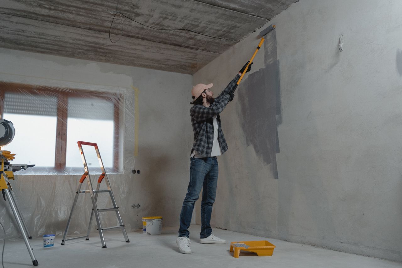 services-04 A man painting an interior wall with a roller as part of a home renovation project.